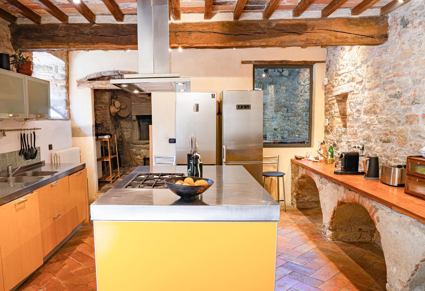 The kitchen with a yellow island, gas range, and stone walls under a beamed ceiling