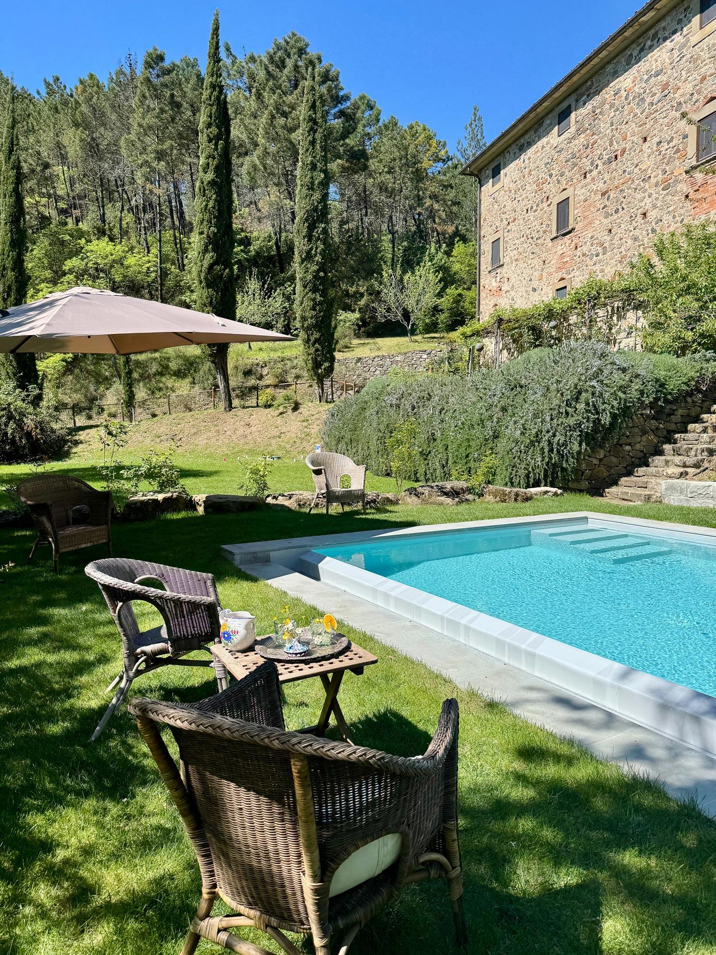 The swimming pool surrounded by lawn and cypresses, the stone facade rising behind