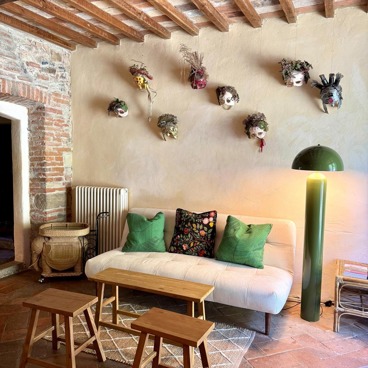 A sitting room with a white sofa, green pillows, and woven masks arranged on the wall