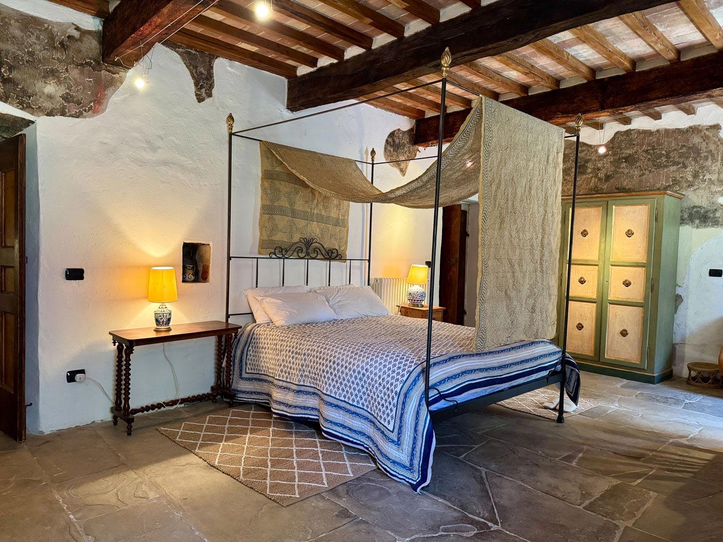 A canopy bed beneath a vaulted ceiling, with a hand-painted wardrobe to one side