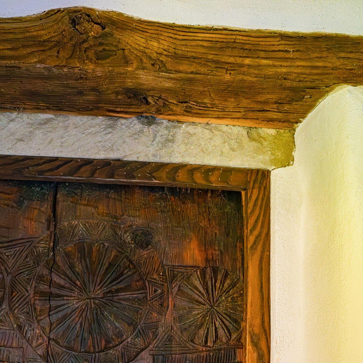 Carved wood door frame with rosette detailing under a hand-hewn timber lintel