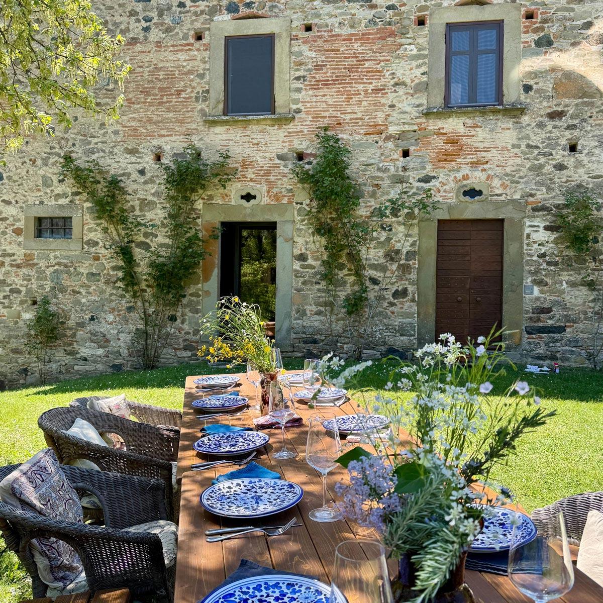 A long outdoor table set with blue-and-white plates, before the stone facade in summer