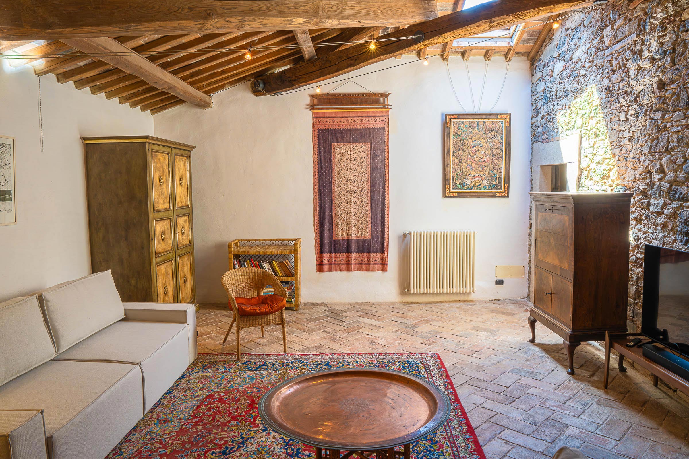 Top floor lounge with a hanging textile tapestry and small icon on the wall, large copper tray on a coffee table, white sofa beside a painted armoire