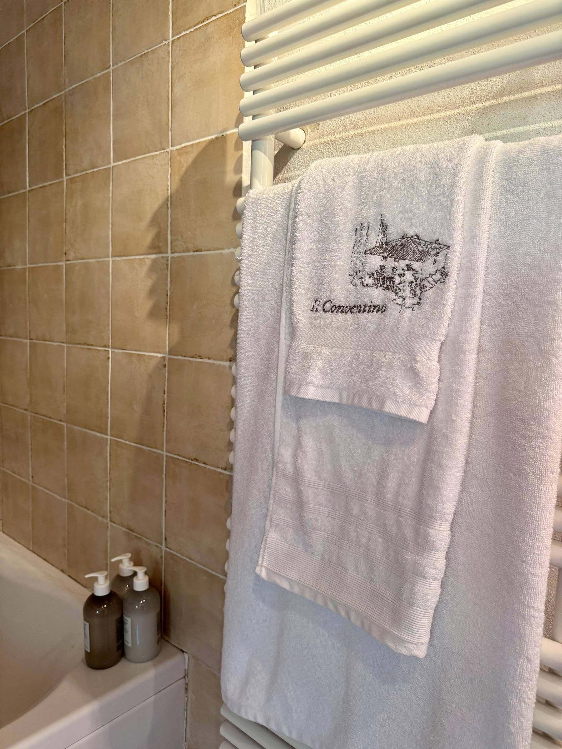 Folded white towels on a heated rail, the smaller embroidered with the Il Conventino monogram