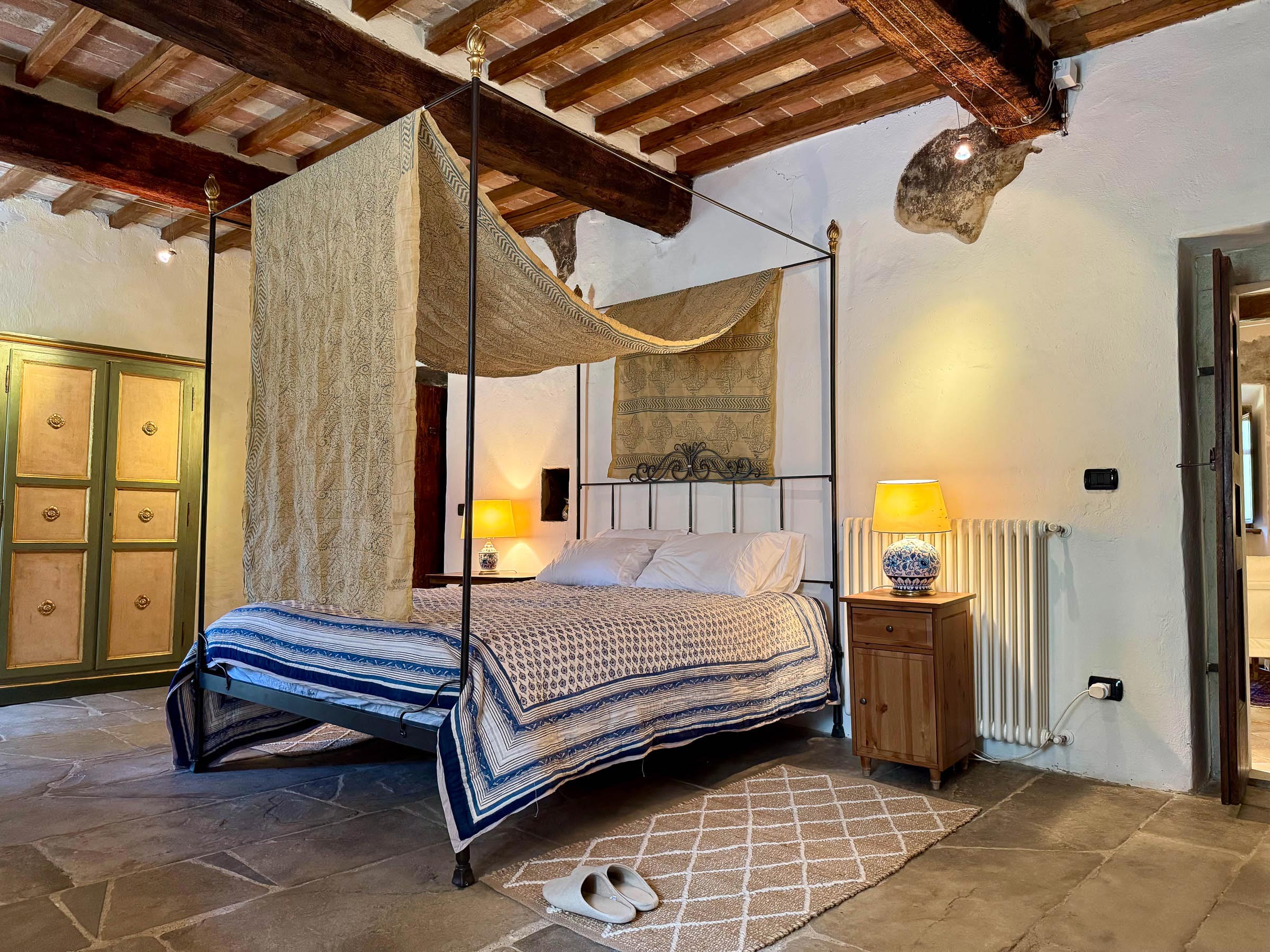 Iron four-poster bed with sheer fabric draped from the canopy, blue-and-cream coverlet, painted armoire and bedside lamps