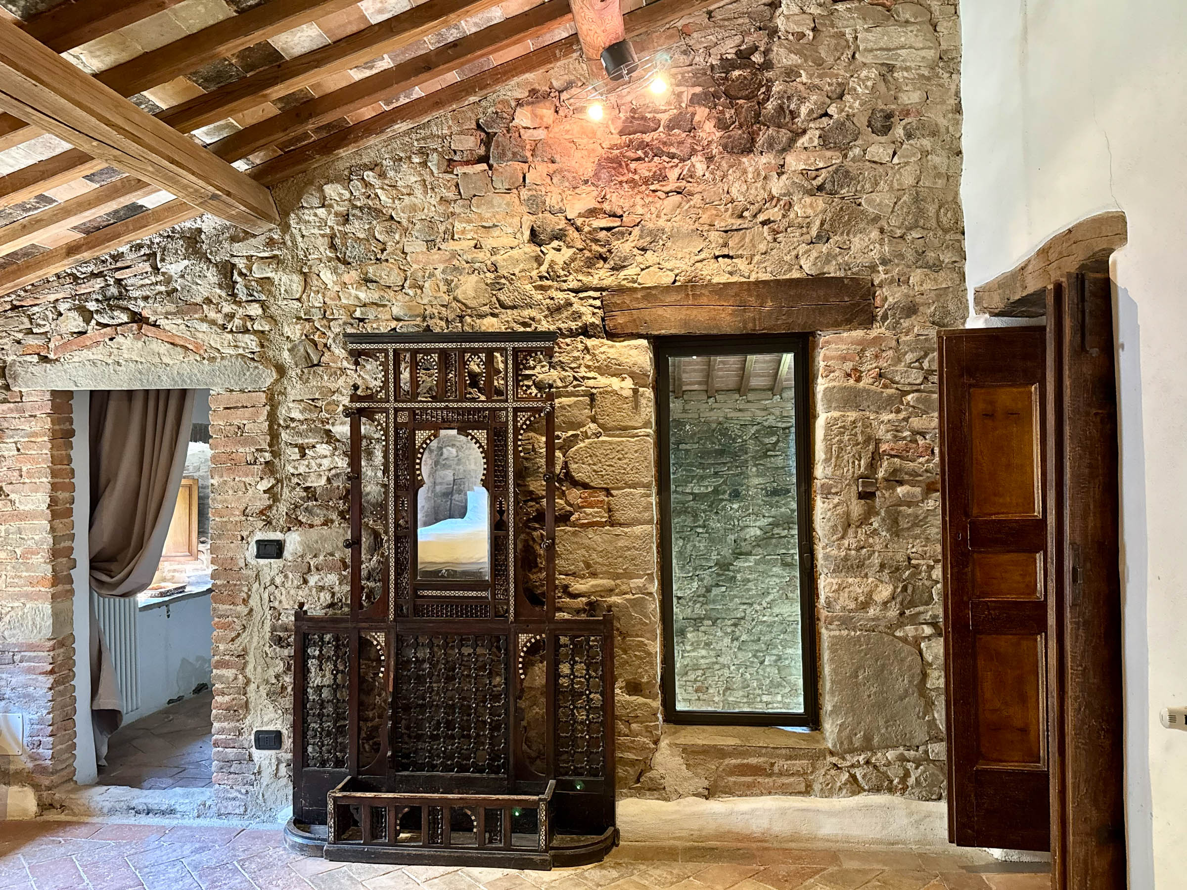 Stone-walled top floor bedroom entryway with an ornately carved Moorish stand and mirror against the back wall, deep recessed window overlooking the chapel from above
