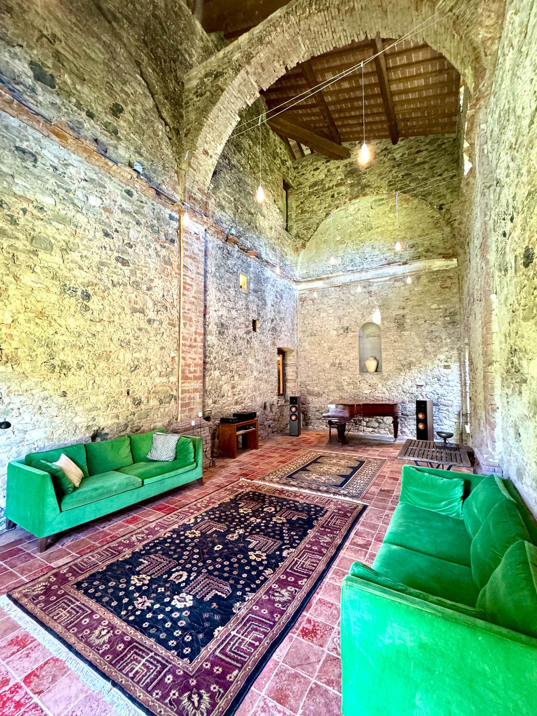 The converted chapel: two emerald-green sofas facing across patterned rugs, a grand piano at the far end beneath a vaulted beamed ceiling