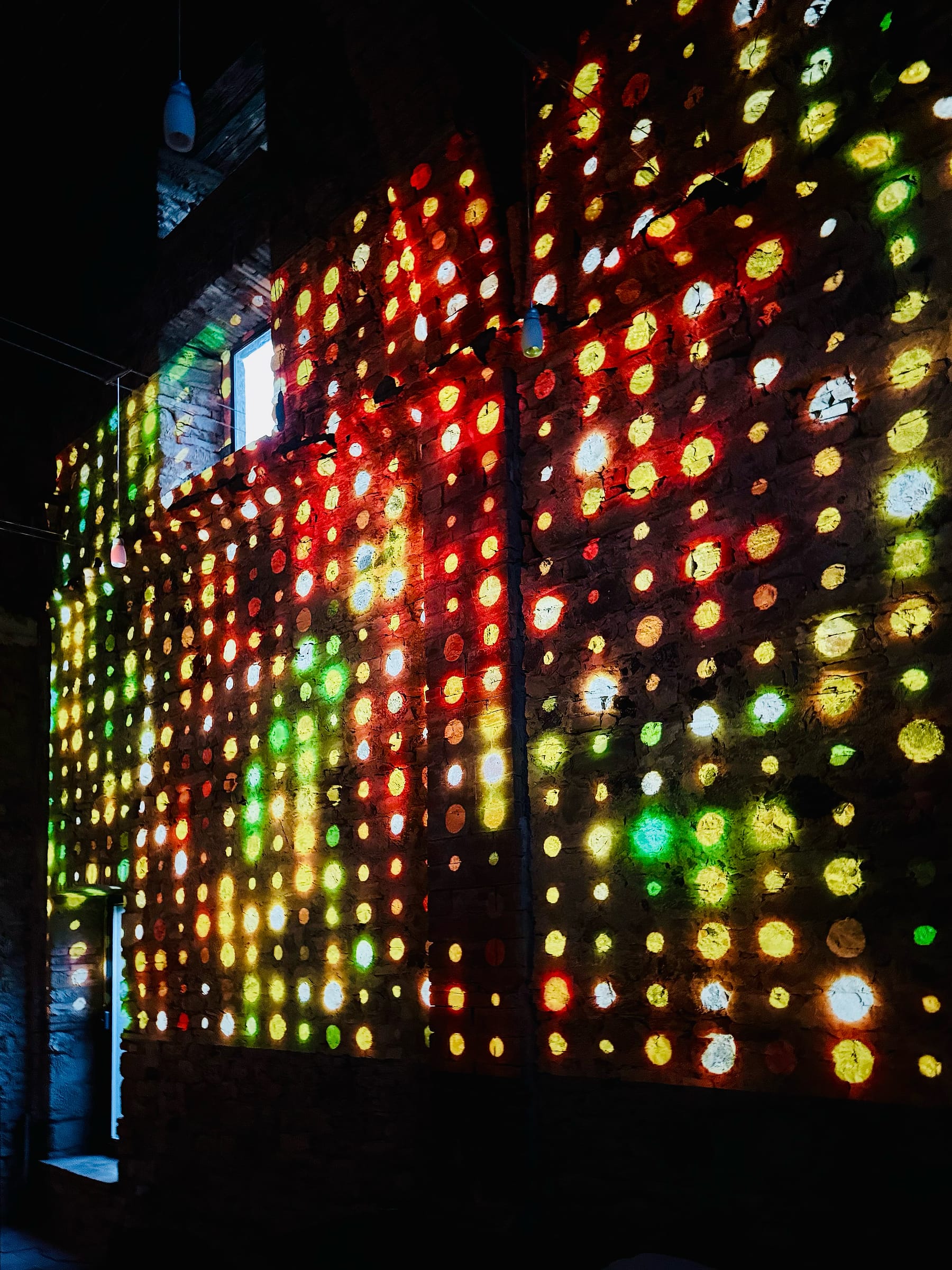 A grid of coloured light projected across the chapel wall in the dark, forming a field of red, green and yellow points