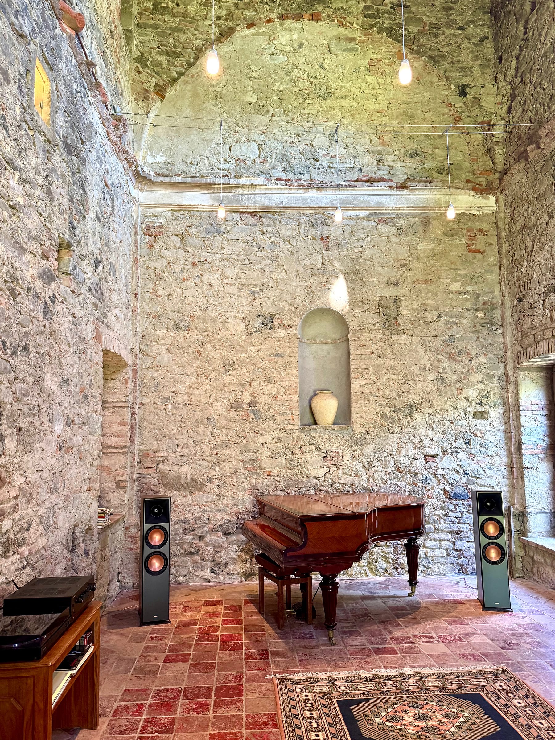 The chapel seen along its length, stone walls rising to a vaulted ceiling, with a baby grand piano at the far end