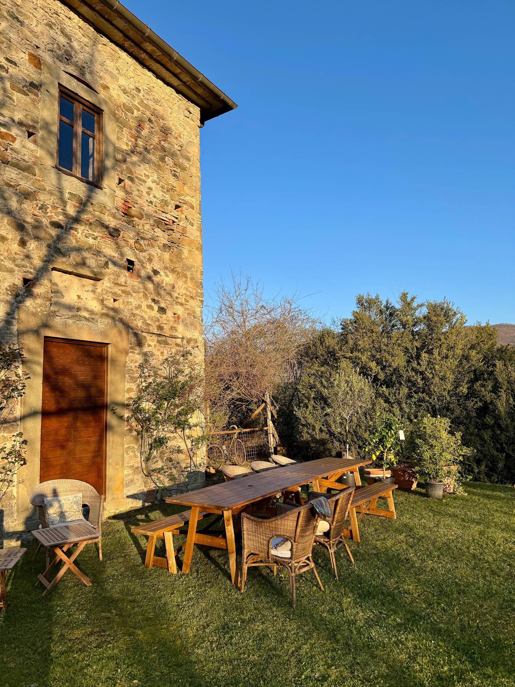 Stone facade of the building beside a long wooden outdoor dining table set up on the lawn, late-afternoon light