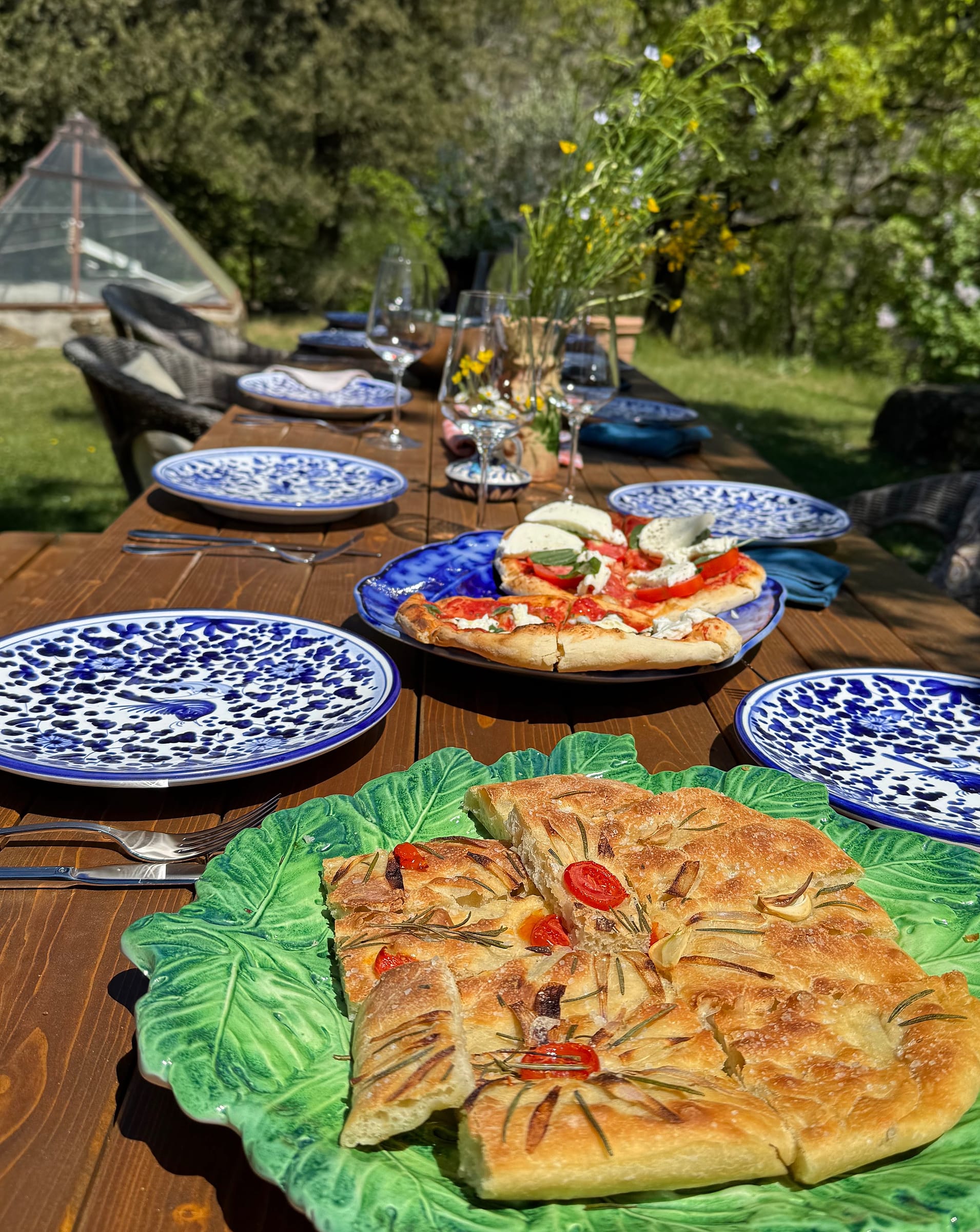 Pizza and rosemary focaccia served on a leaf-shaped platter at a long outdoor table laid with blue-and-white plates