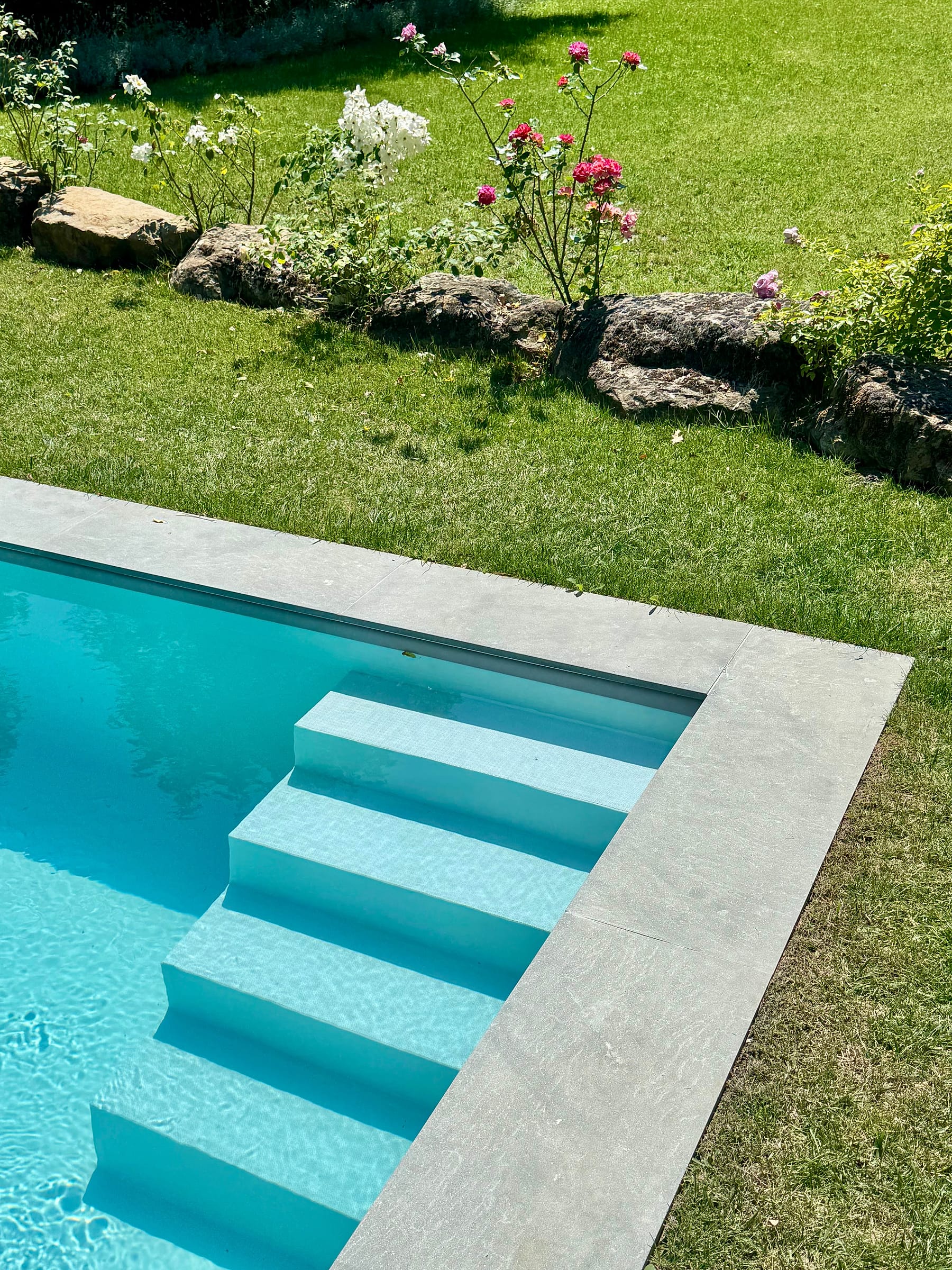 Submerged steps in one corner of the pool, roses and mown lawn along the stone coping