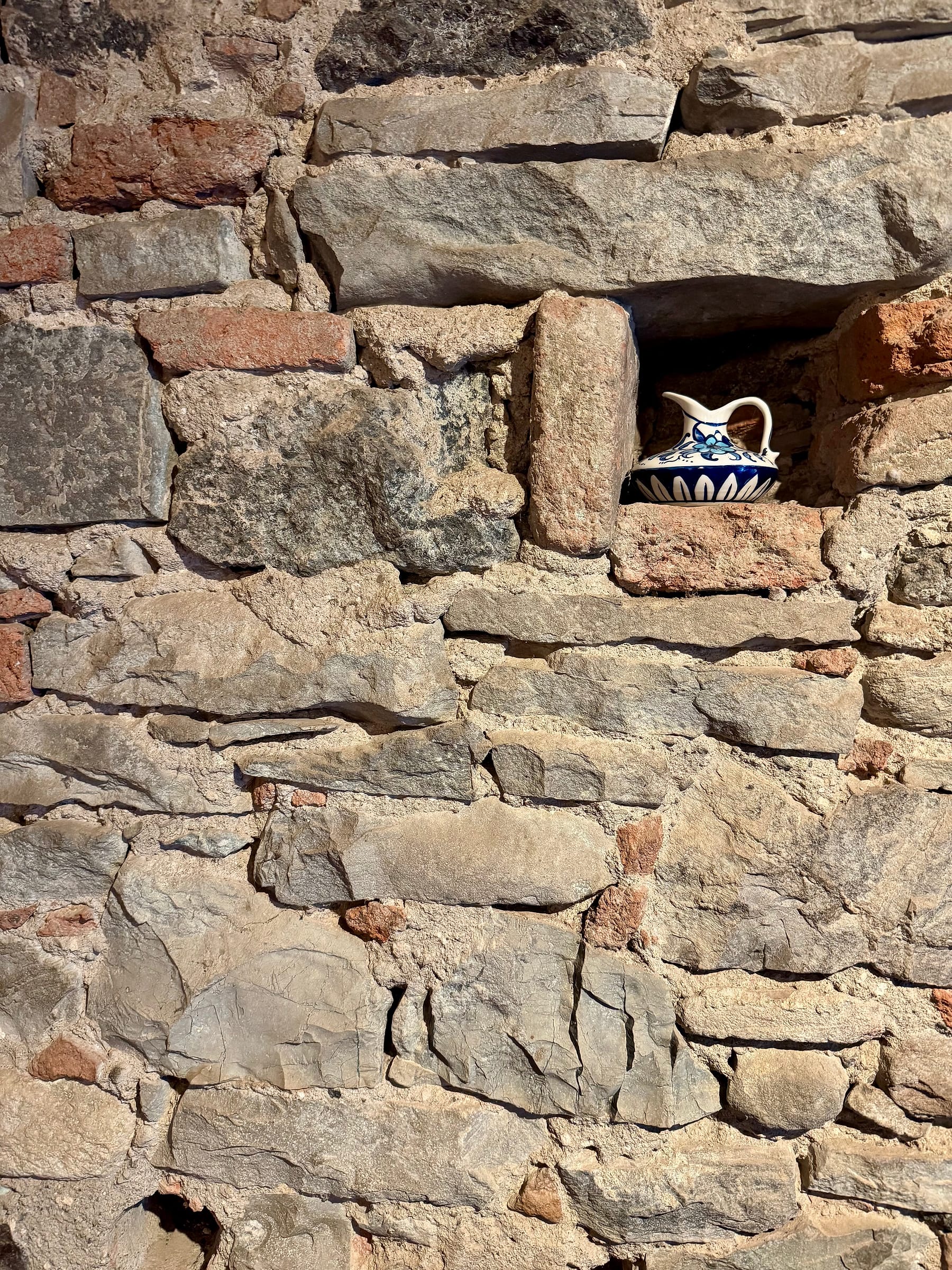 A blue-and-white ceramic jug standing in a small niche in a wall of rough, irregular stonework